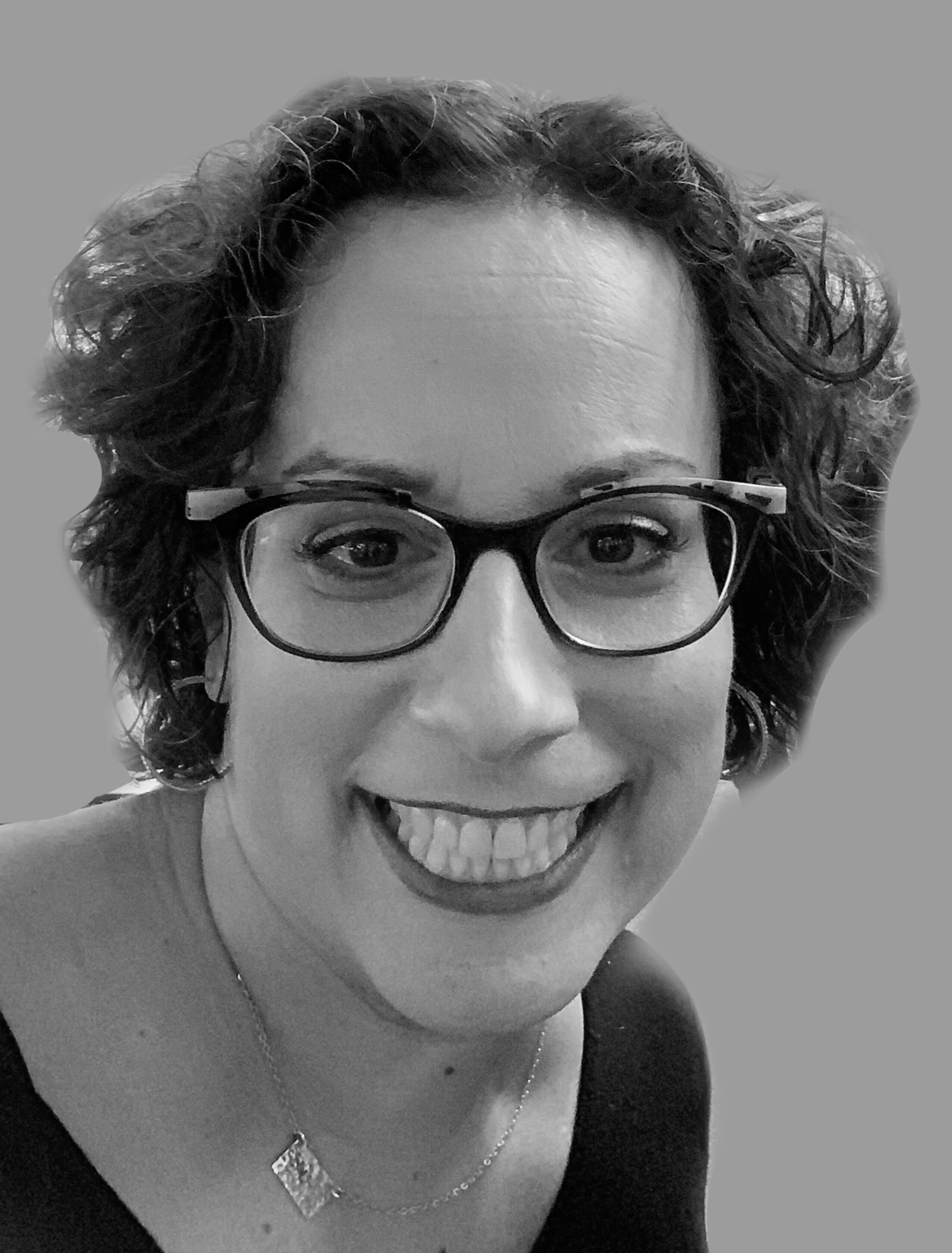White woman with short curly hair and dark rimmed glasses smiles at camera
